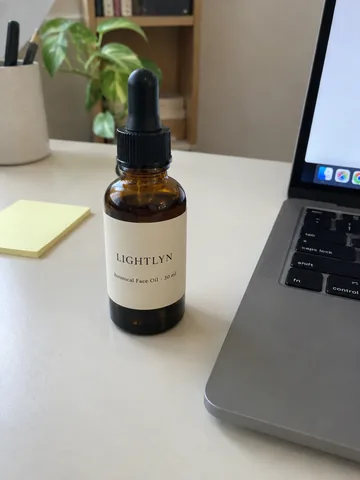 Original: an amber dropper bottle labelled LIGHTLYN Botanical Face Oil 30 ml on a desk next to a laptop